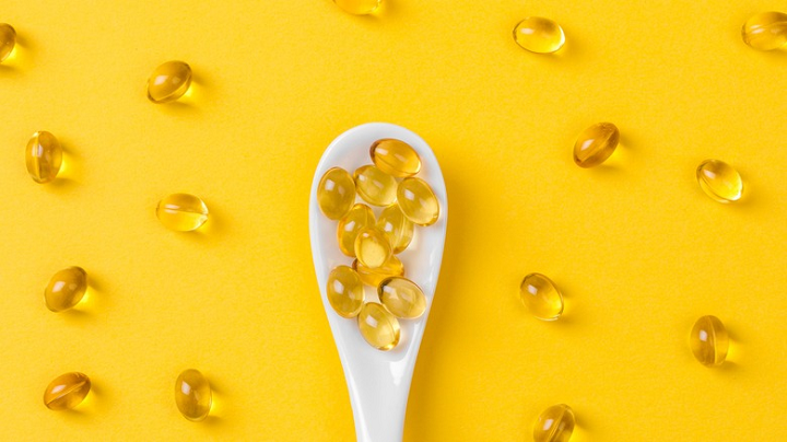 Vitamin capsules in a white spoon on a yellow background.